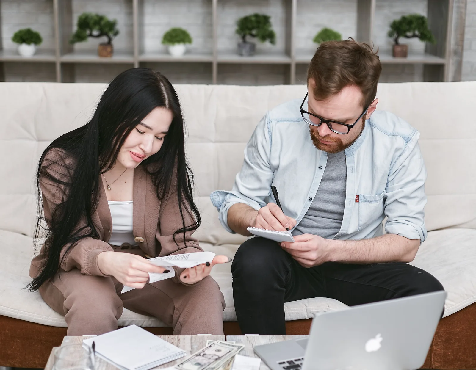A man and woman sitting indoors, reviewing expenses with notebooks and money on the table. Bank of Canada payment system dates: Lynx windows and holidays