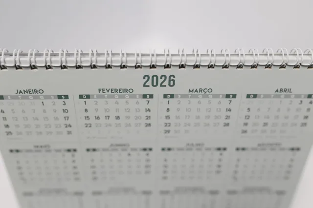 Close-up of a 2026 spiral-bound desk calendar with months in Portuguese. Days between dates holidays: past and future windows