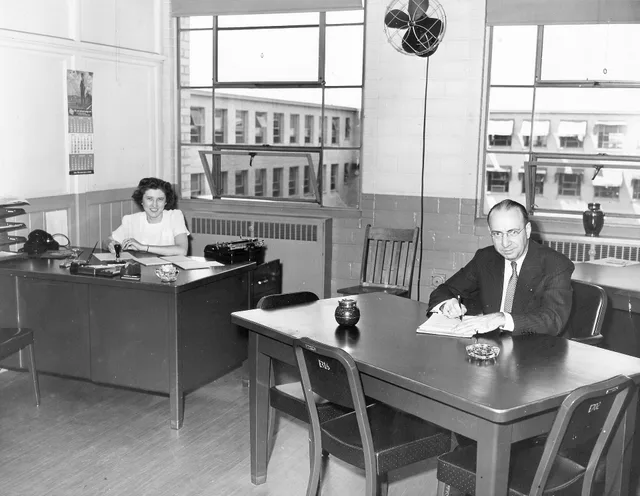 "Office of the Commanding Officer, Twin Cities Ordnance Plant, St. Paul, - Minneapolis", Minnesota. Shows office at Twin Cities Ordnance Plant that was located in New Brighton, Minnesota during World War II. The man seated at desk is "engineering manager" Raymond M. Winslow. Woman at left is unident. Subtract business days formula: WORKDAY and worked cases